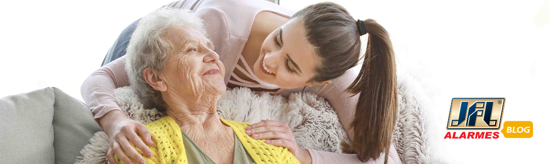 Mulher jovem e alegre demonstrando carinho por uma idosa sentada na poltrona.